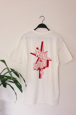 White t-shirt with a pink and red design that says “Ranch Rider Spirits Co.” on the back.