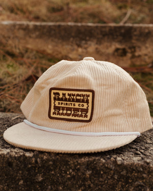 Cream-colored corduroy baseball hat with a tan and brown patch on the front that says “Ranch Rider Spirits Co.”