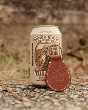 Leather keychain leaning against The Buck product. The keychain has a "Ranch Rider" logo embossed.
